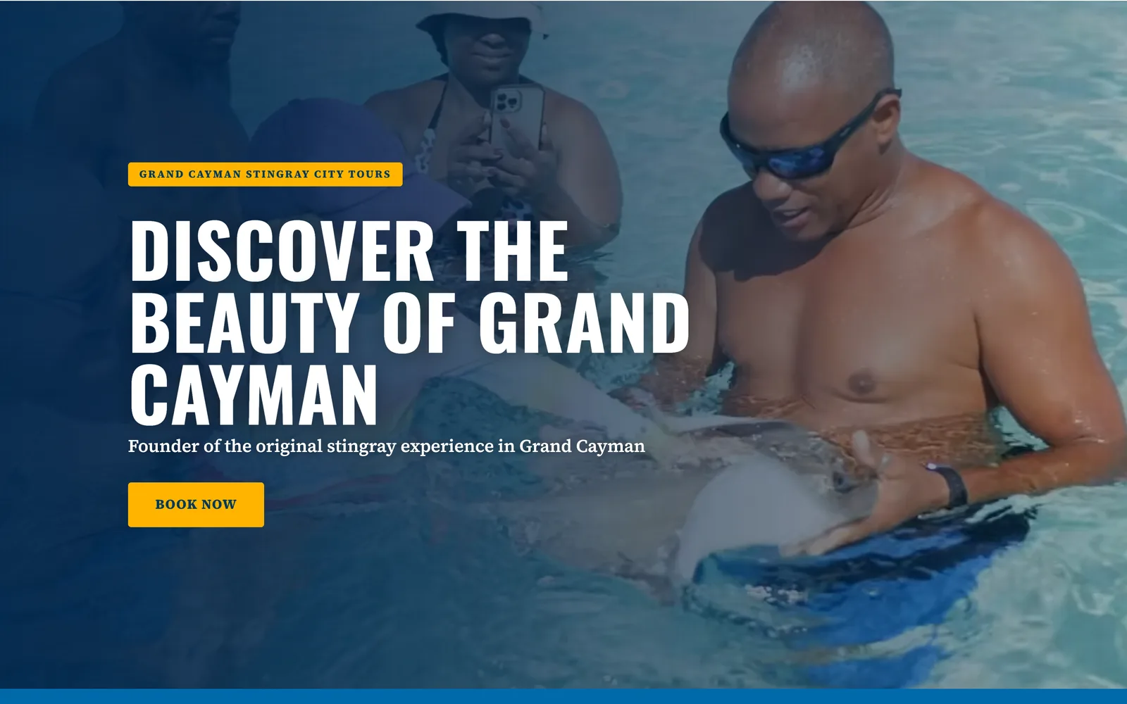 Home page of a watersports website on a laptop: a guest holding a stingray in clear water, white capitals and a yellow Book now button