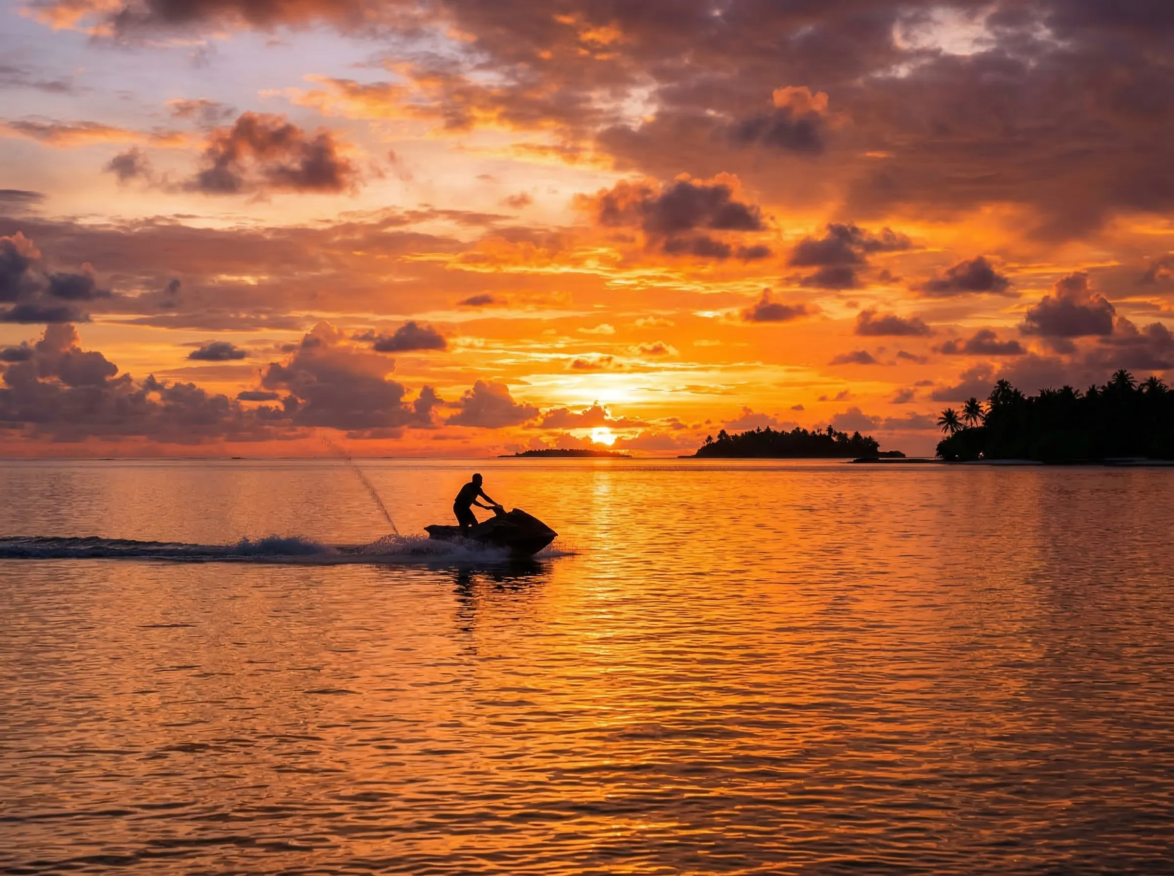 Lone jet skier silhouetted against tropical sunset