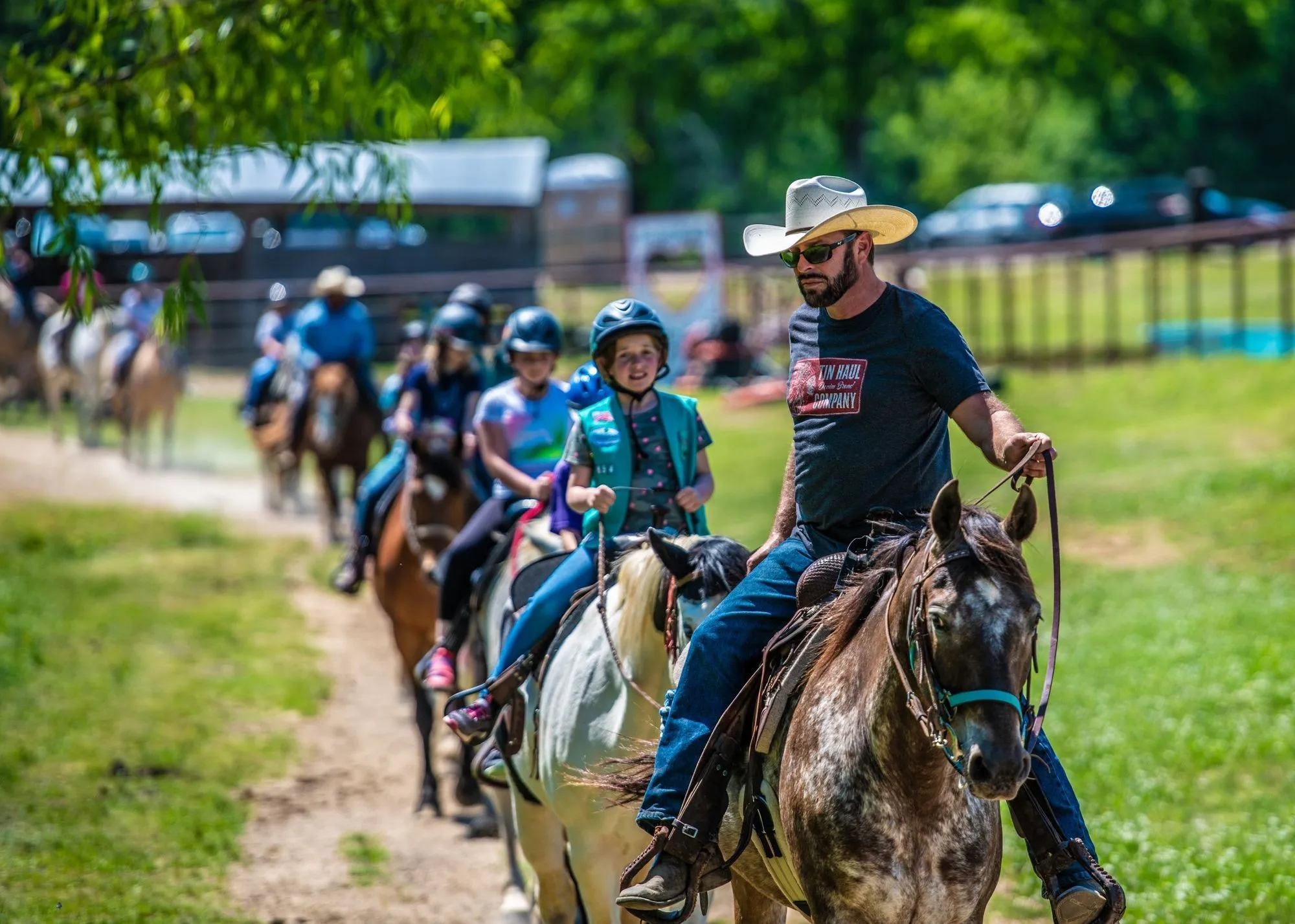 A guide in a cowboy hat leading kids on a horseback trail ride