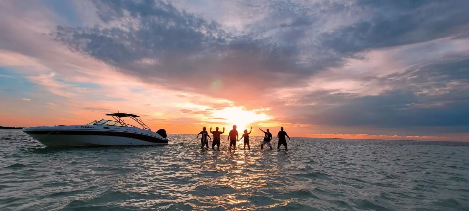 Key West Boat Trips guests standing in the water at sunset, arms raised