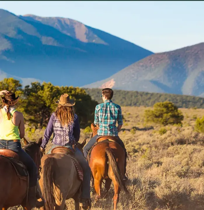 Three guests riding horses through the mountains with Rio Grande Stables